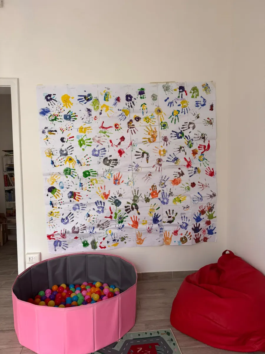 Parete decorata con le impronte delle manine colorate dei bambini, piscina di palline e pouf