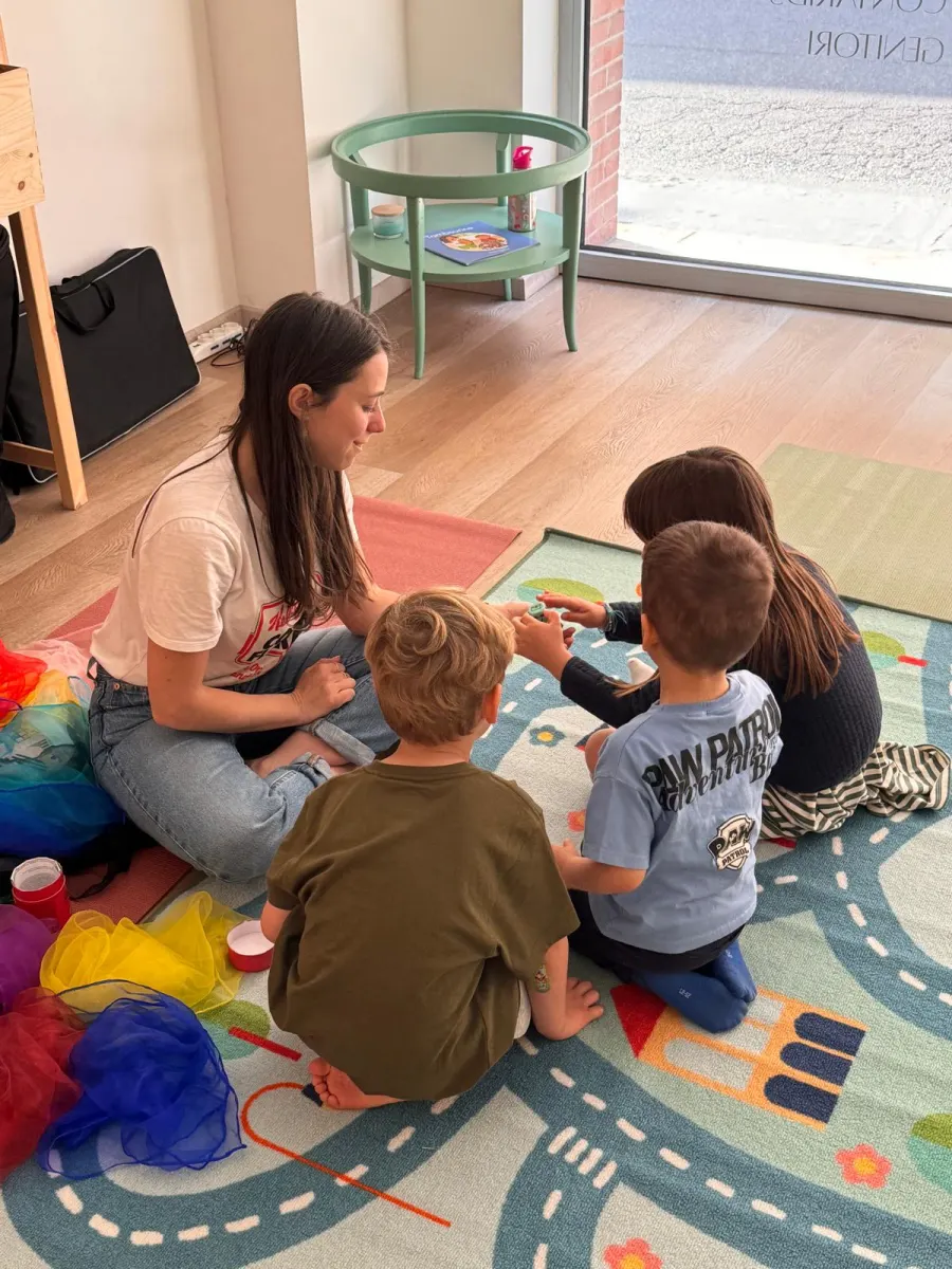 Susie e tre bambini seduti sul tappeto gioco, tra foulard colorati